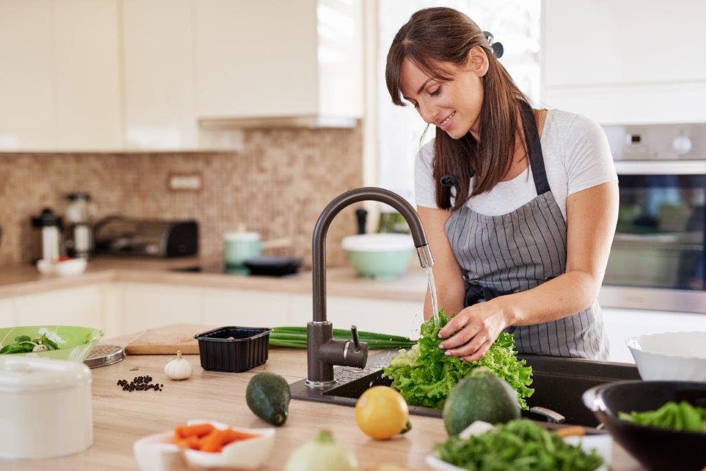 A woman washing lettuce in the kitchen sink