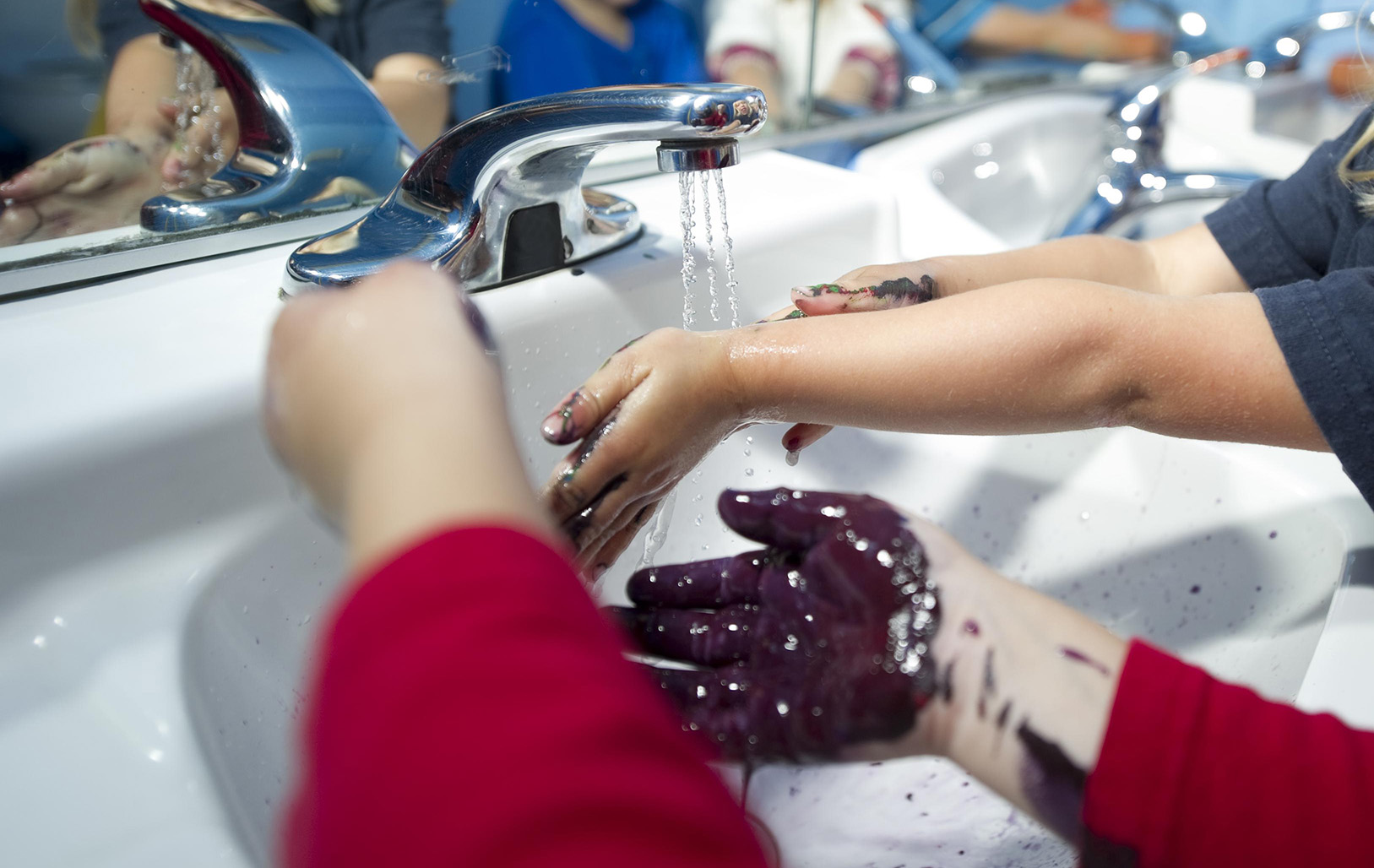 Kids with paint on their hands washing their hands in a sink