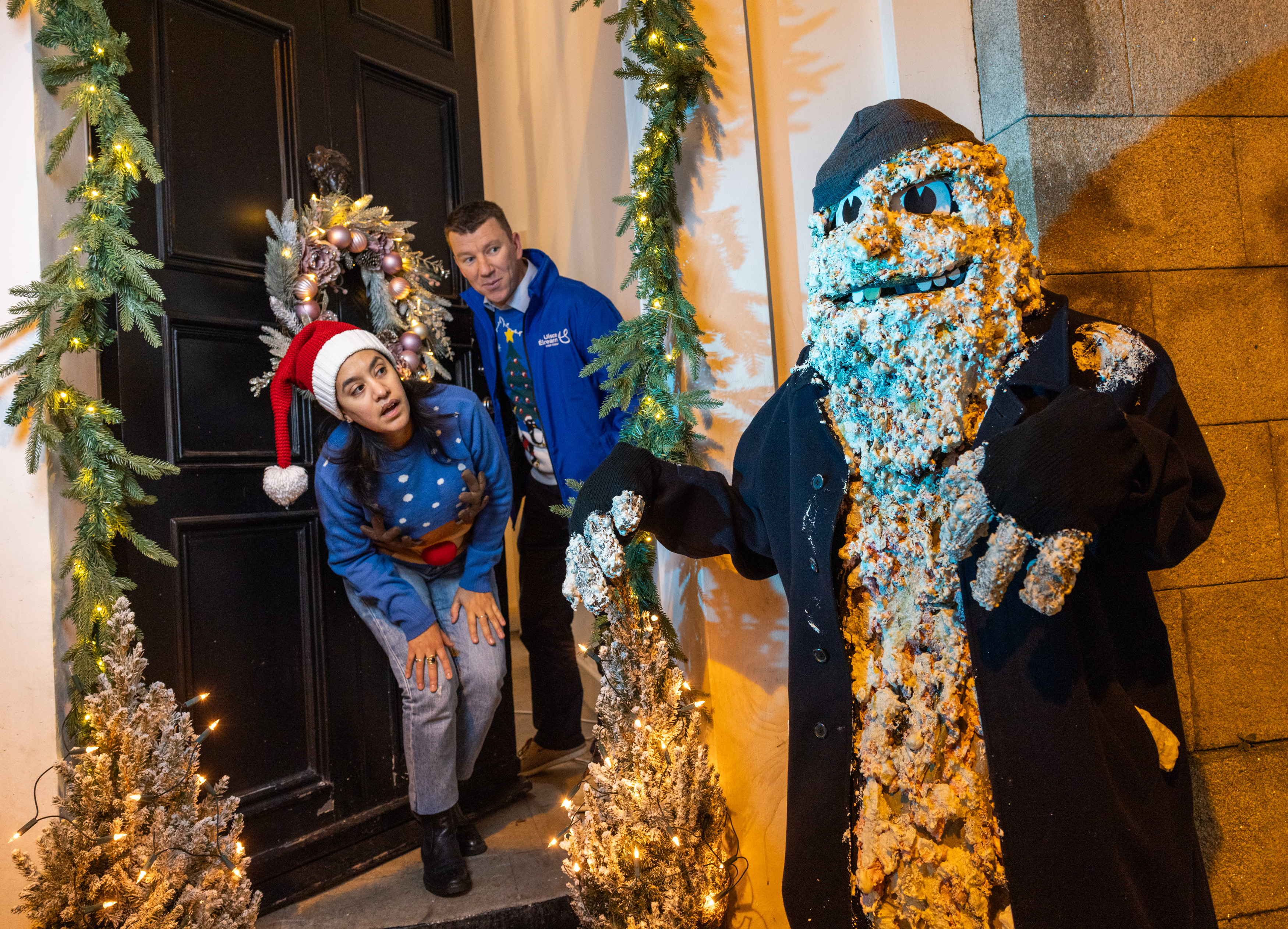 Two Uisce Éireann workers in Christmas jumpers looking out a door at a scary mascot