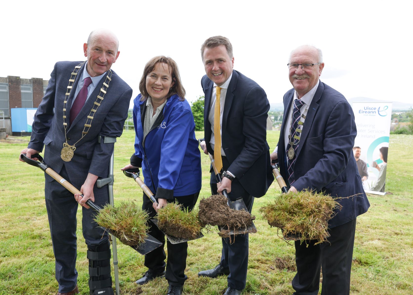 Four people holding shovels with grass on them and smiling at the camera