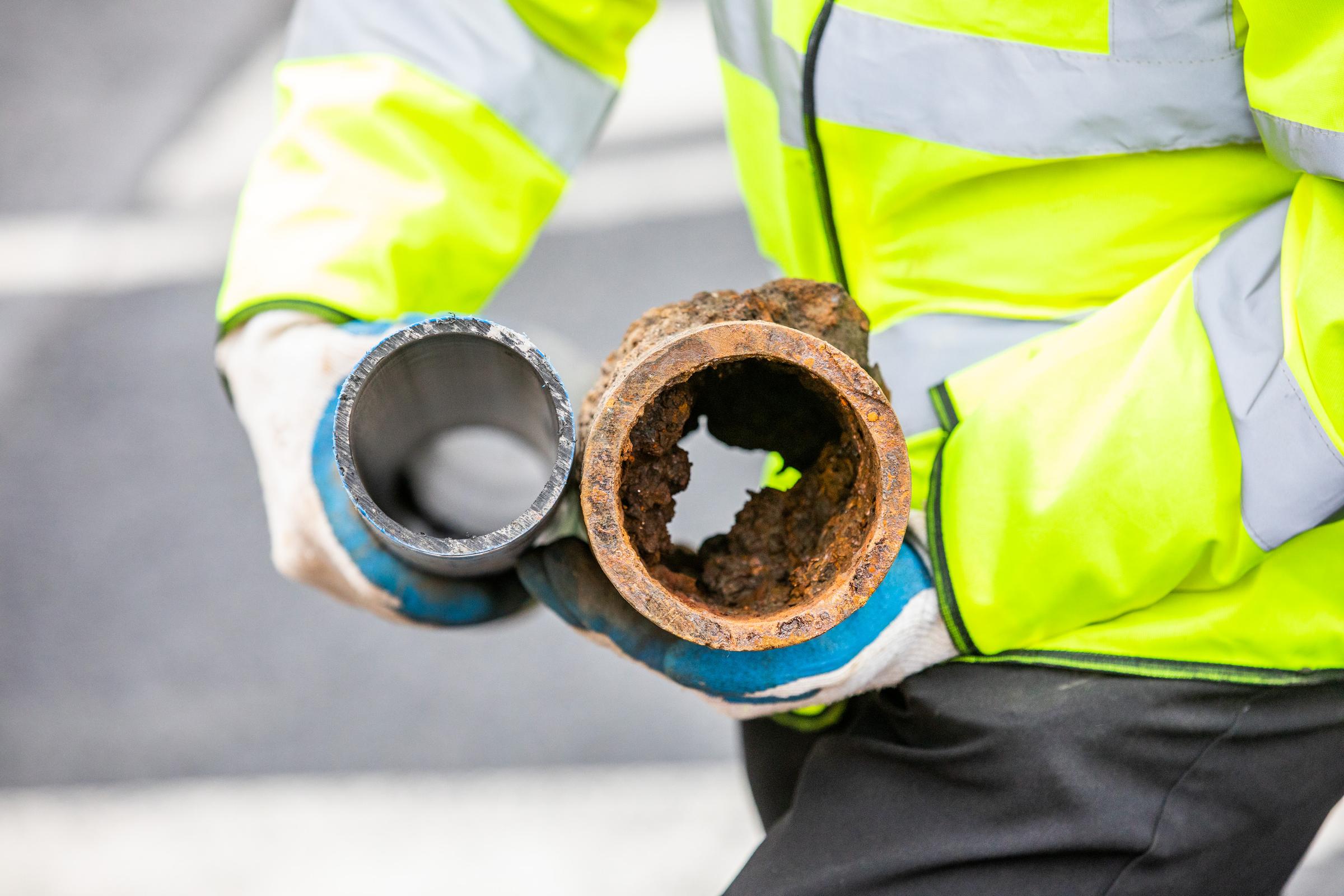 A worker holding a new clean pipe and an old damaged and rusty pipe