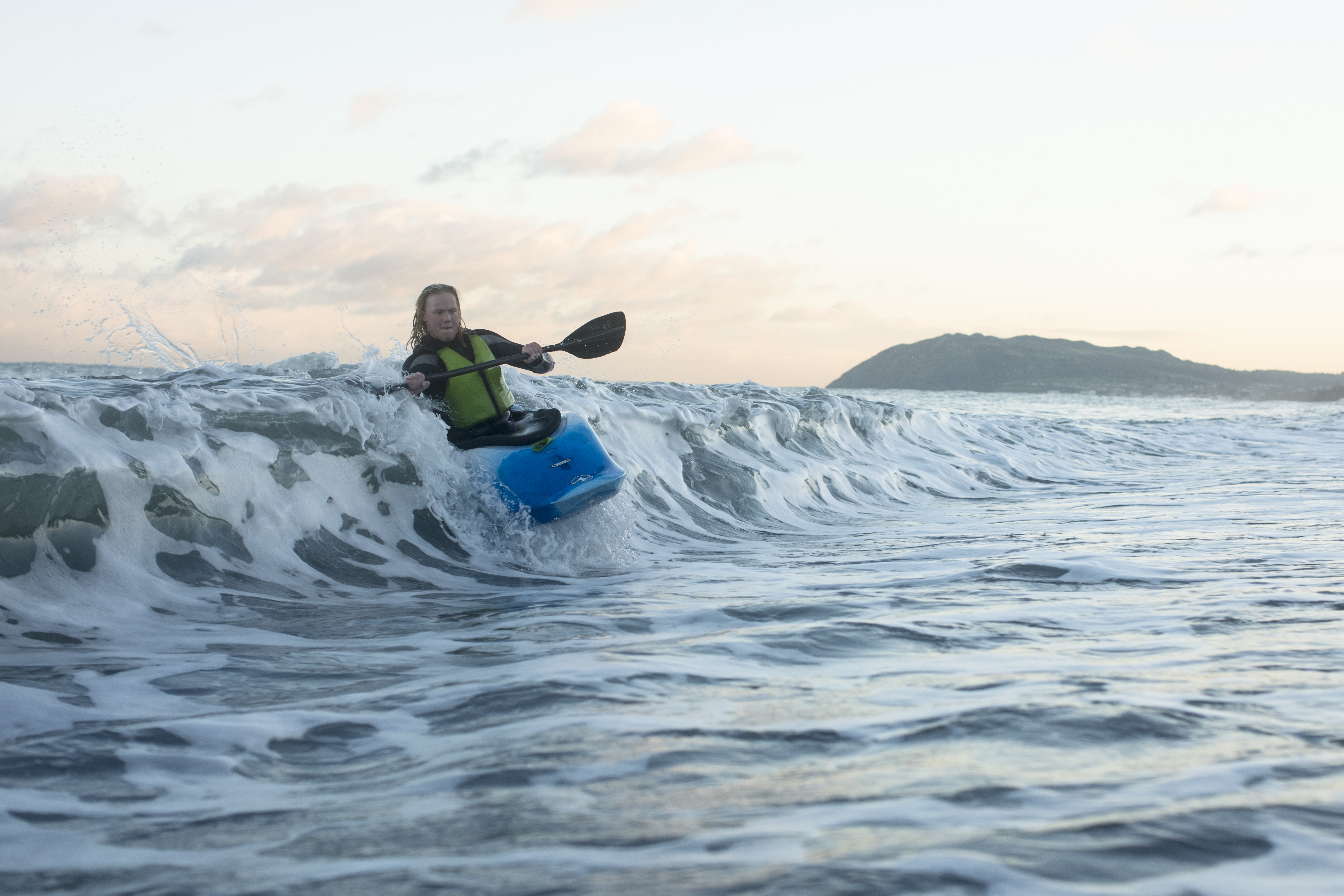 A woman in a blue kayak riding a wave