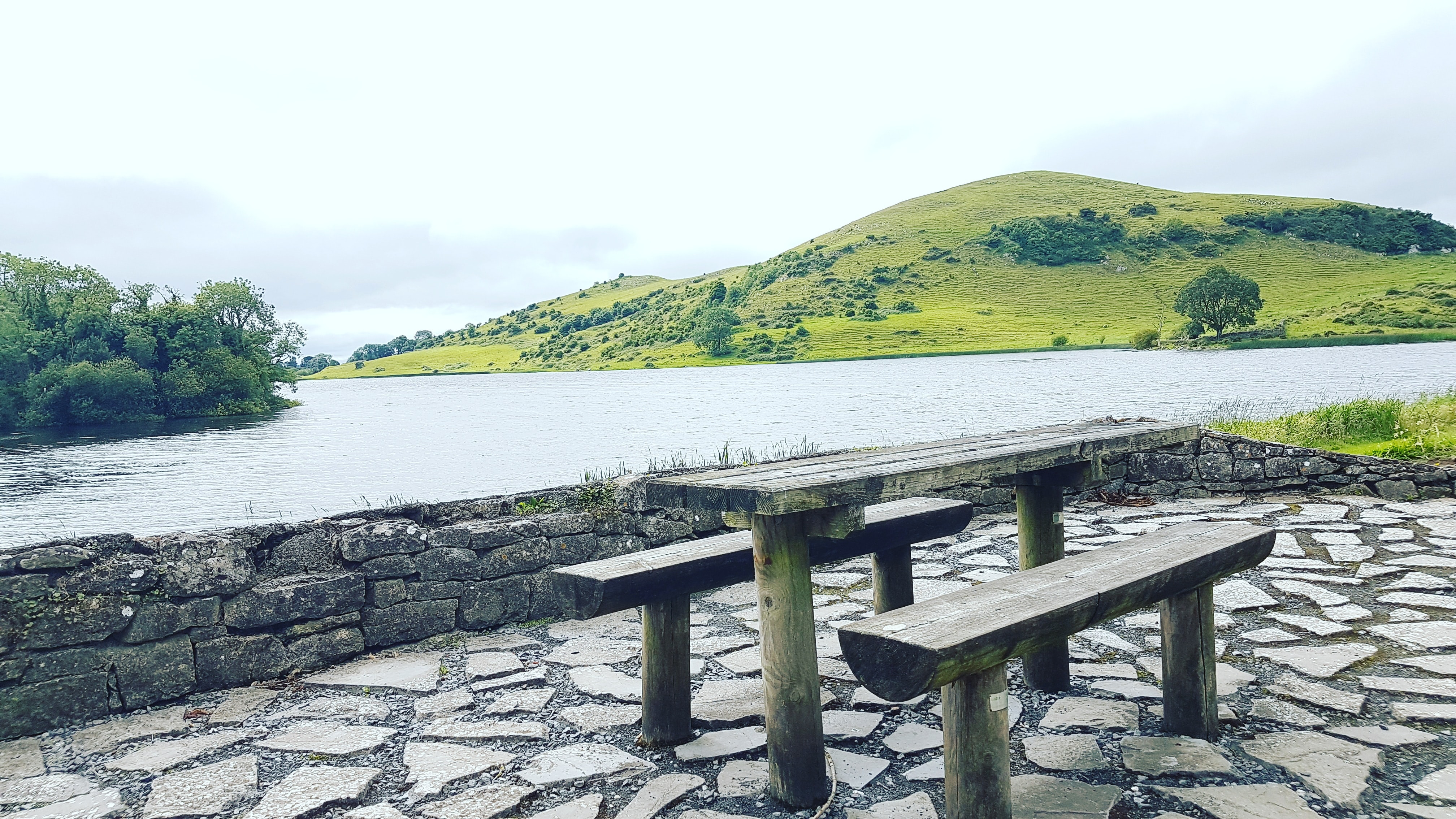 A picnic bench by a lake and a grassy hill