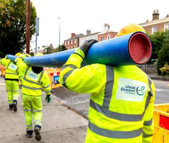 Three Uisce Éireann Engineers carrying a blue pipe in a road work