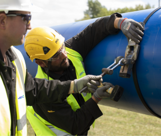 Two Uisce Éireann workers working on a large blue pipe